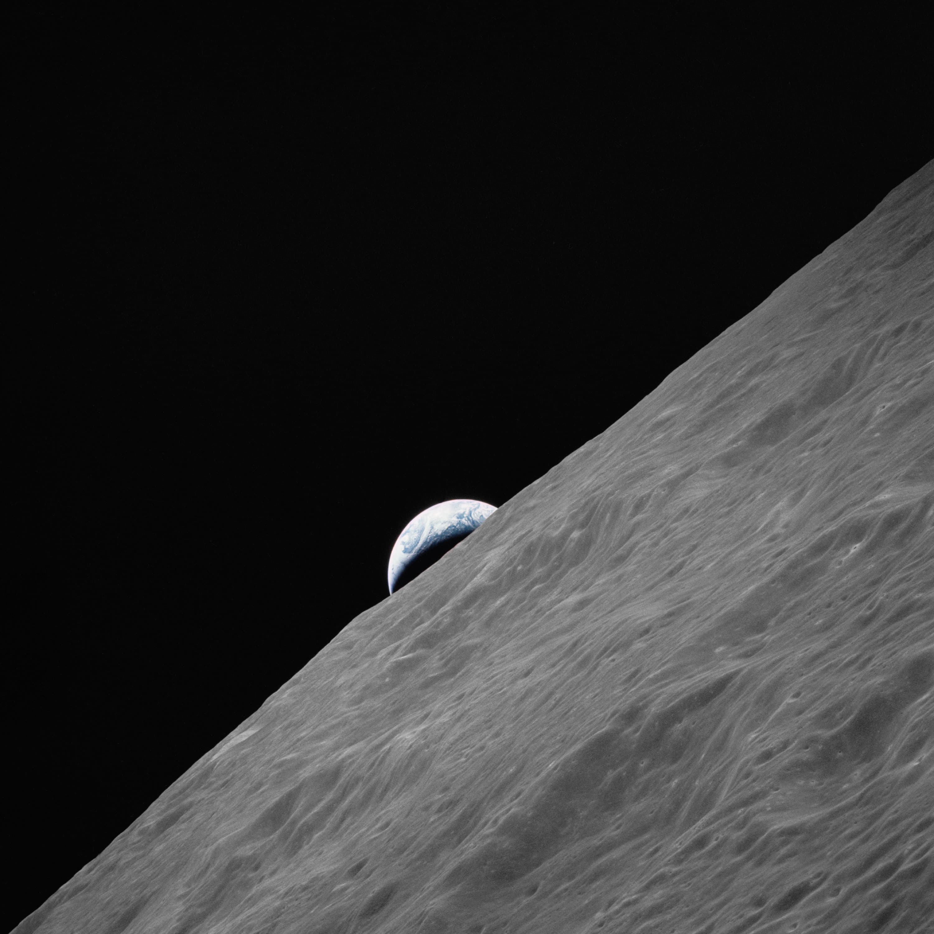 A blue crescent Earth rising above the grey lunar horizon, photographed during Apollo 17.